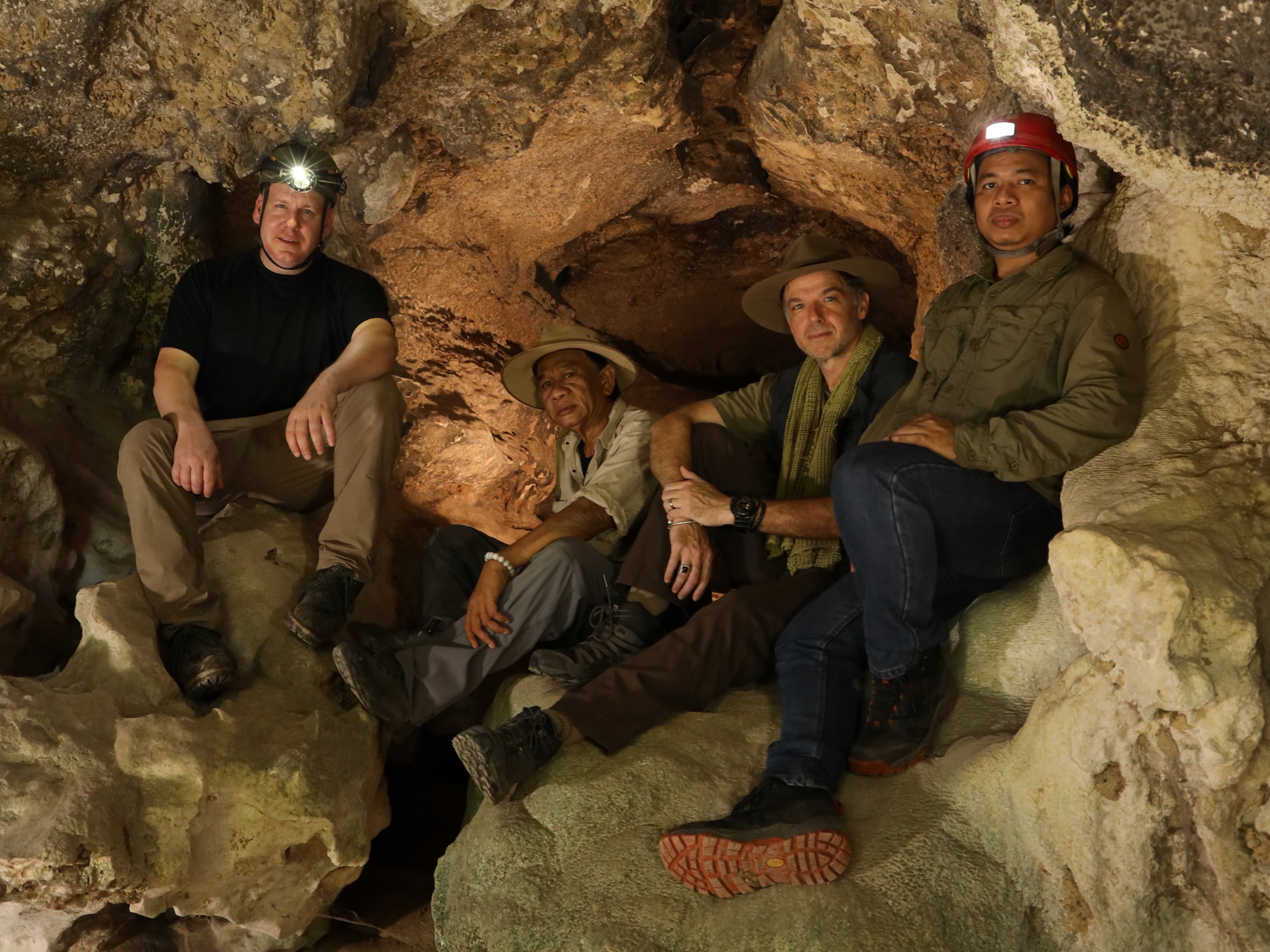 Four archaeologists wearing headlamps sitting inside an Indonesian cave