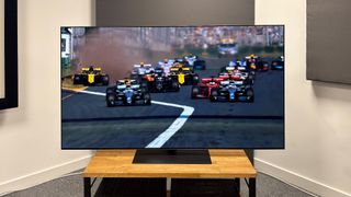 The 65-inch LG G5 OLED TV pictured on a wooden rack. On the screen is a still from Netflix F1 series Drive to Survive.