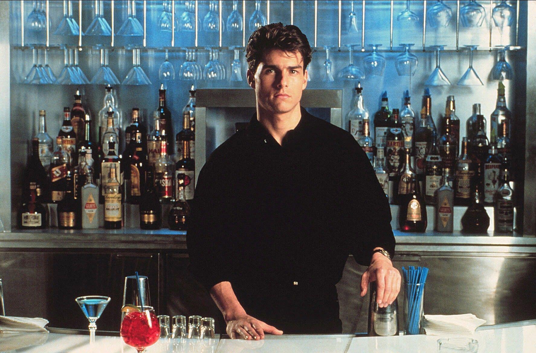 Tom Cruise at a bar in the film Cocktail, surrounded by glassware and alcohol