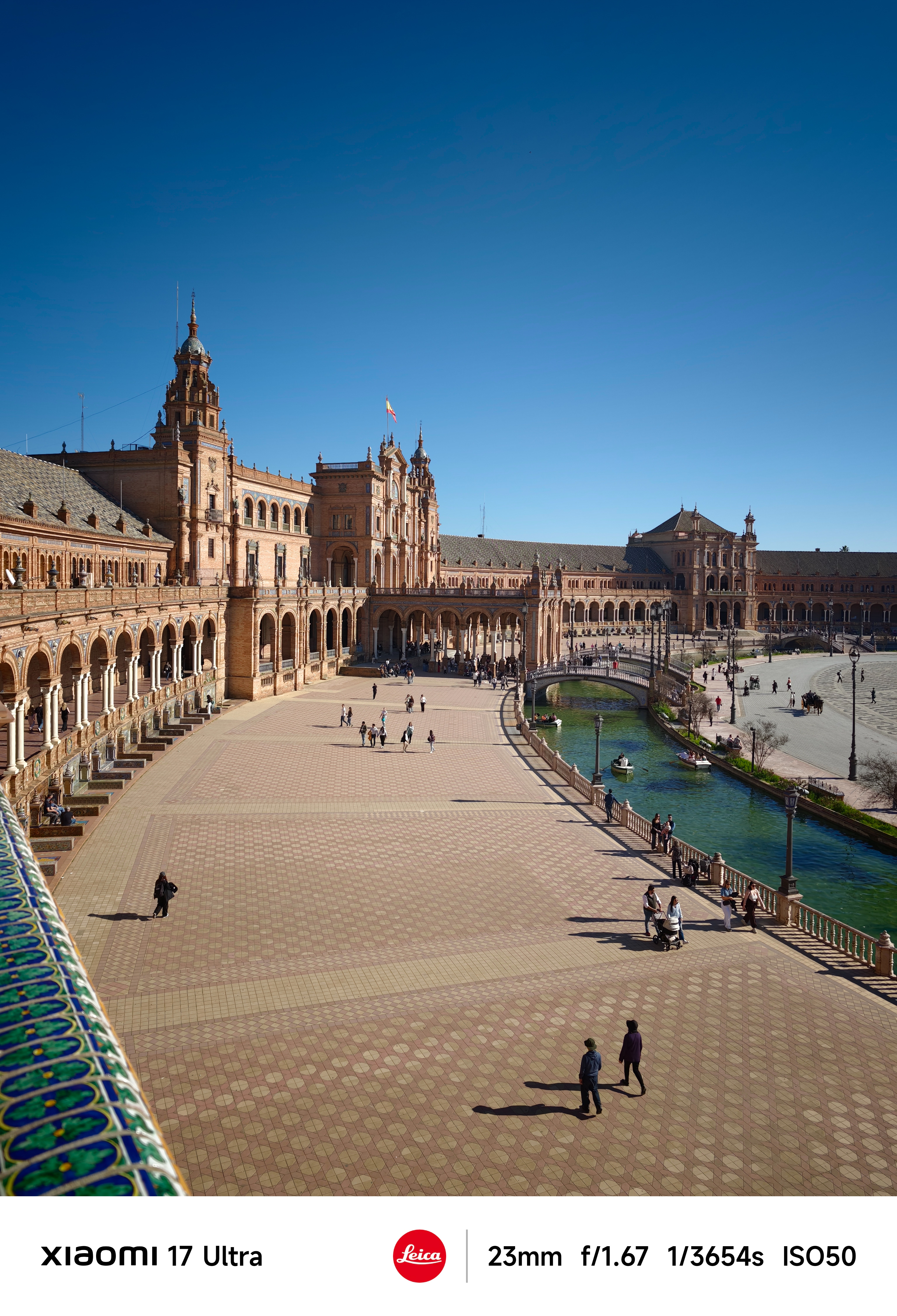Wide view across Plaza de España’s tiled square and canal under a cloudless sky.