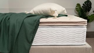 Saatva Organic Quilted Mattress Topper on top of a Saatva mattress with a green sheet draped over it and a pillow on top; it's discounted in the after Christmas mattress sales