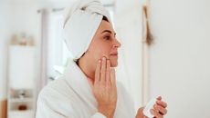 Mature woman in a bathroom at home applying dark spot serum - stock photo