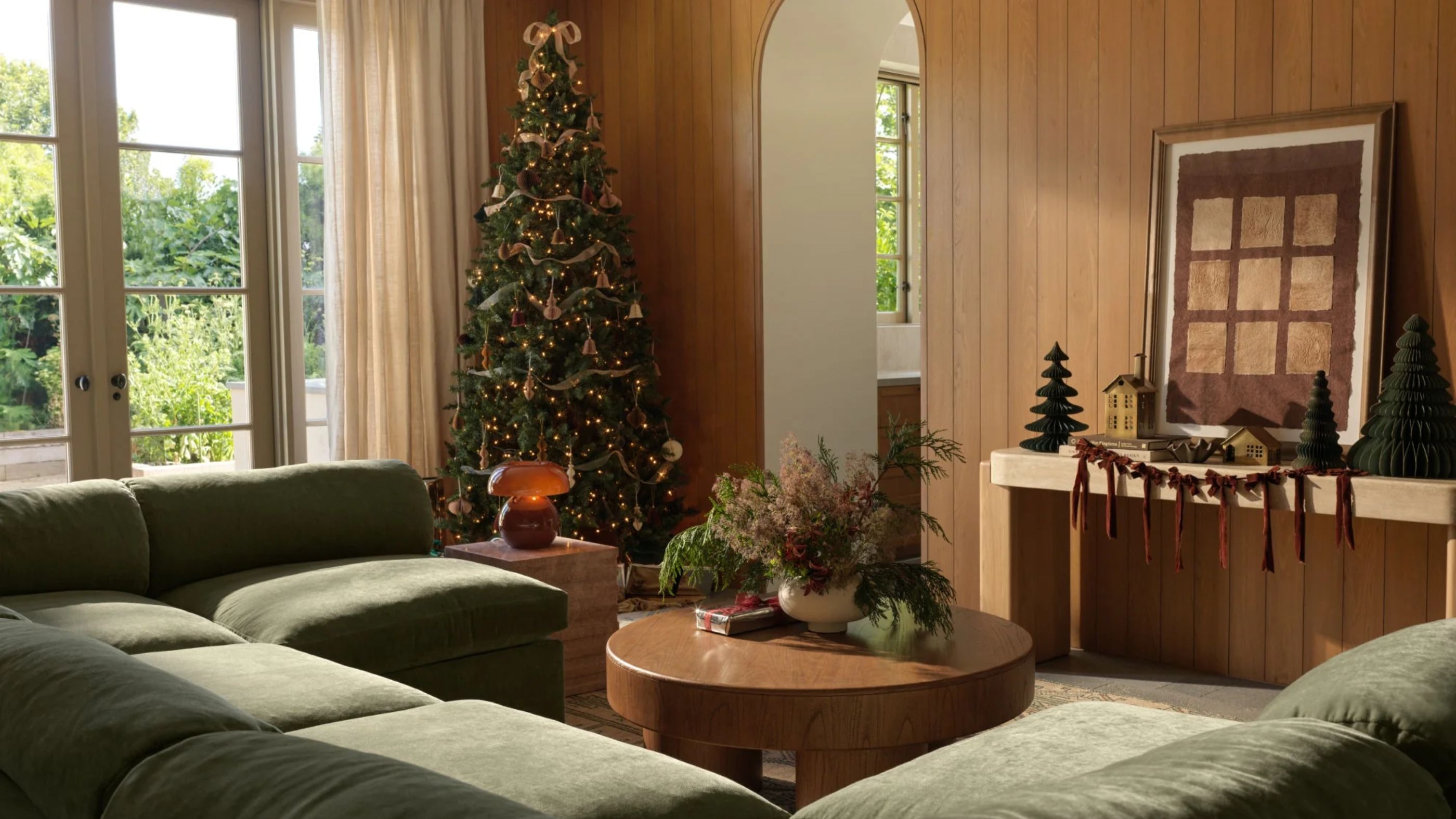 wooden panelled living room with a green modular couch dressed for christmas with a tree