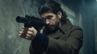 Ben Whishaw in Black Doves holding a gun up and looking down the barrel.