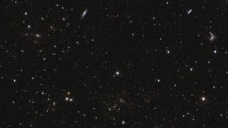 A sea of stars and galaxies sparkle against a black background. Several galaxies can be identified by their elongated shape and/or spiral arms. Some galaxies are seen edge-on while one prominent spiral galaxy at the bottom centre is seen face-on. At the far right, between the middle and top of the image, are some interacting galaxies. Galaxy clusters are also seen, in particular near bottom centre, where features smeared into arcs represent gravitational lensing. The brightest stars in the image have diffraction spikes