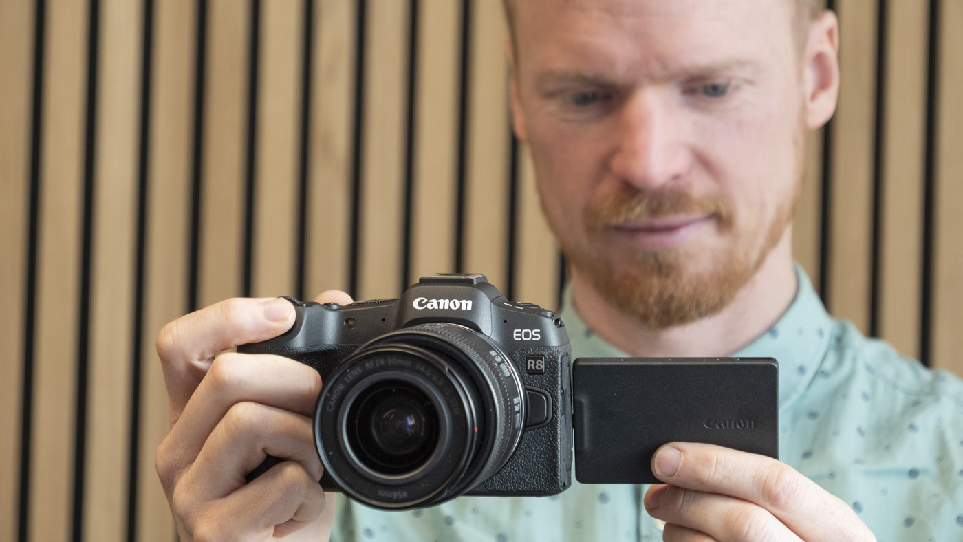 Canon EOS R8 in the hand with vari-angle screen flipped out and photographer looking at the screen