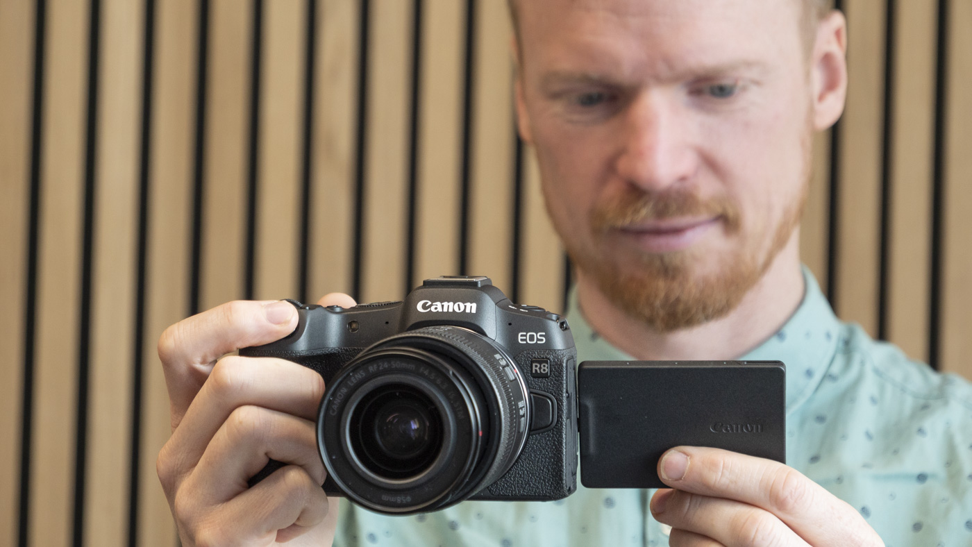 Canon EOS R8 in hand, multi-angle screen flipped, photographer looking at the screen