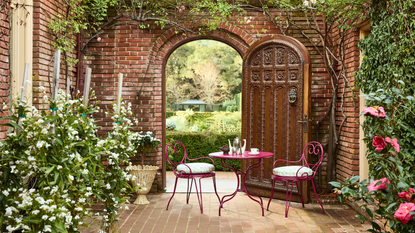 a courtyard with brick walls, a large wooden door, and a red bistro set