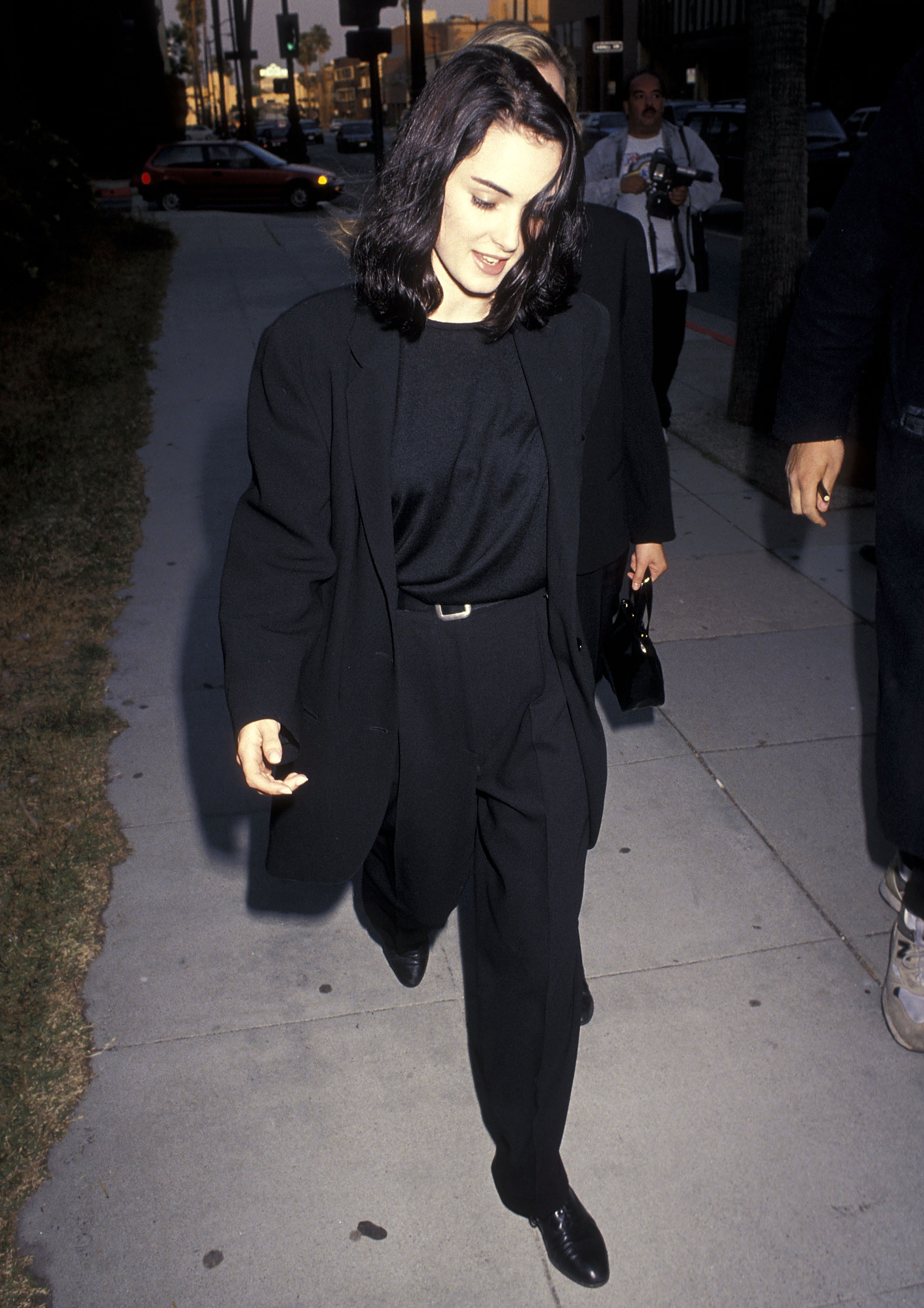 An image of Winona Ryder wearing a black t-shirt, oversized black blazer, black wide-leg trousers and black derby shoes in 1991.