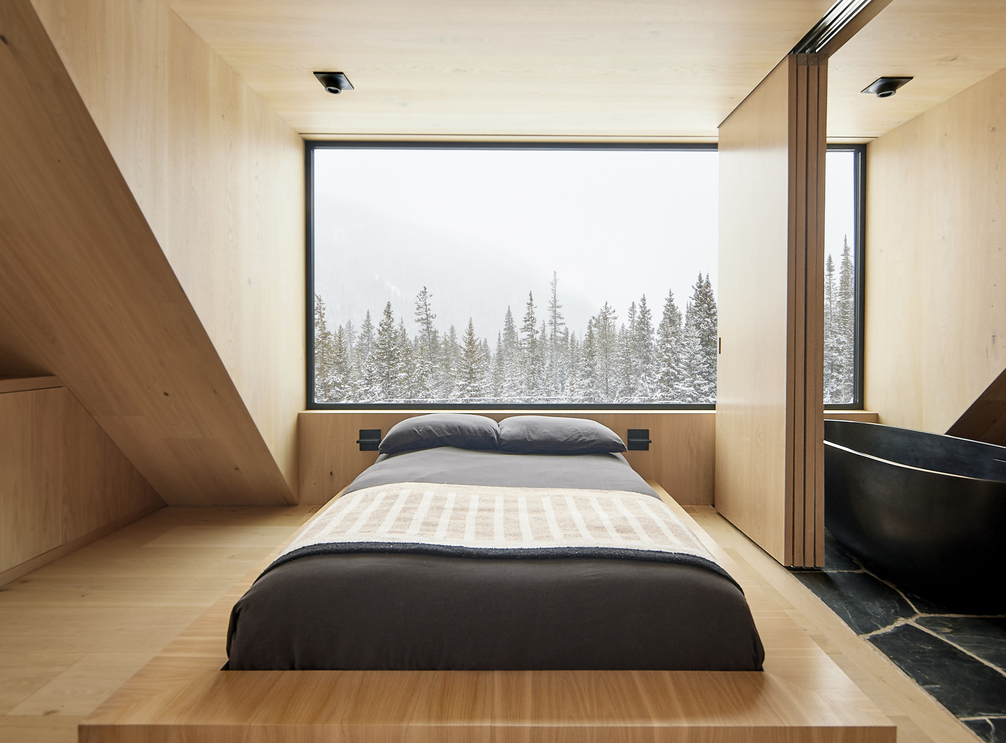 Bedroom clad in white oak with a built-in sunken bed with dark grey bed linen