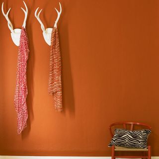 orange wall with animal head hanger red cloth and red chair with designed cushion