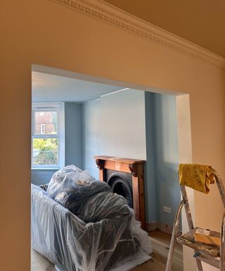 a blue color drenched living room with a wooden fireplace seen through a doorway of a dining room painted in a soft yellow with a darker yellow ceiling