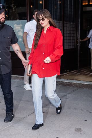 Dakota Johnson is seen in Tribeca on September 05, 2024 in New York City wearing a red button-down shirt, light-wash Levi's jeans, and black loafers.