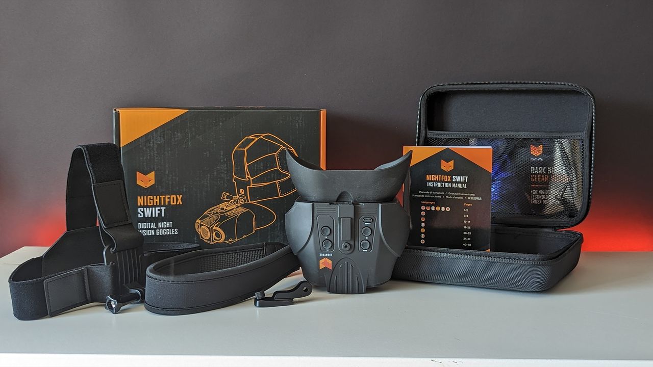 The binoculars with all accessories and box on a white table with a black backdrop