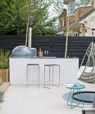 A white outdoor kitchen with black painted fence and slim metal patio furniture.