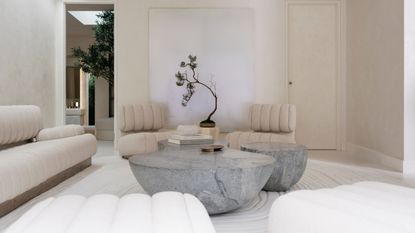 Image of a luxury neutral living room. There are modern accent chairs and a matching sofa with two gray marble coffee tables in the center.