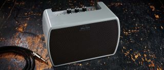 Harley Benton JAMster Guitar: the super-portable practice amp, finished in grey plastic, sits on a distressed wooden floor.