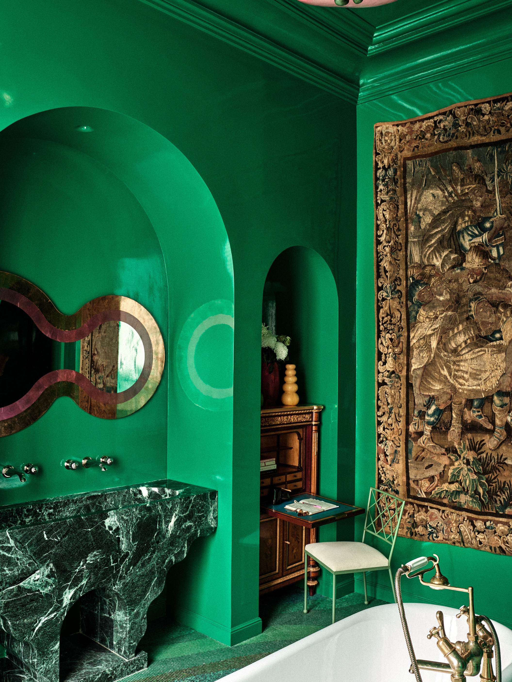 a green bathroom with a green marble sink and antiqued furniture with a large tapestry on the wall