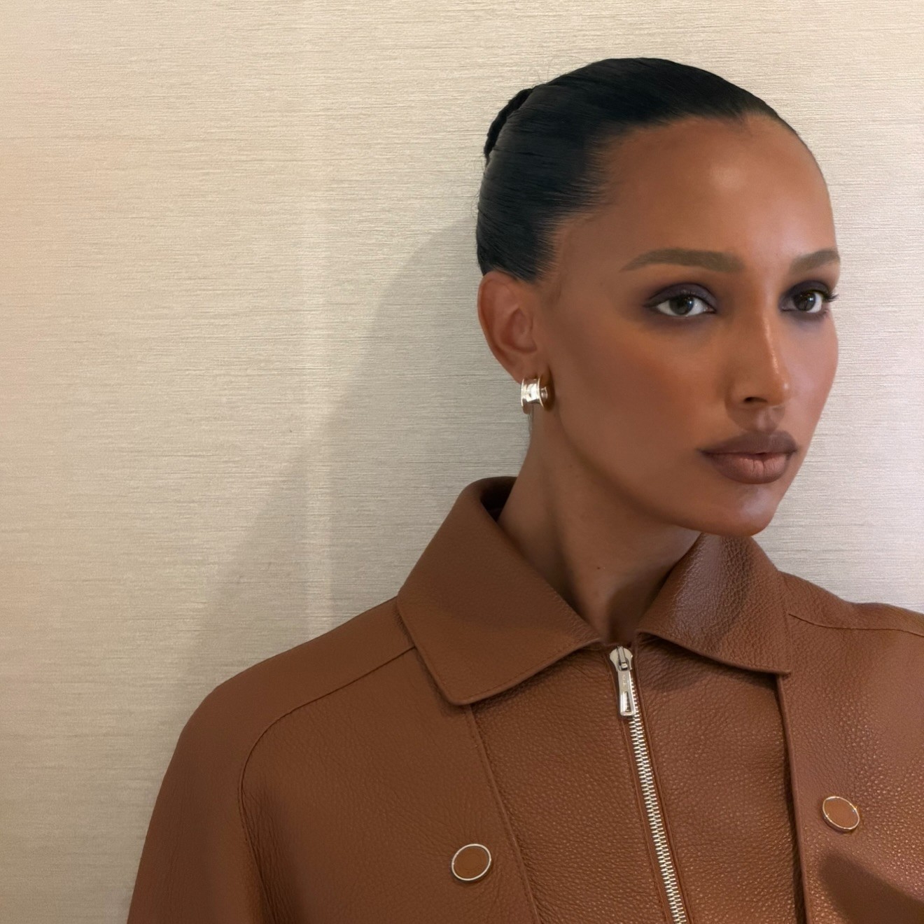 Photo of Jasmine Tookes wearing a brown jacket with hair slicked back into a bun