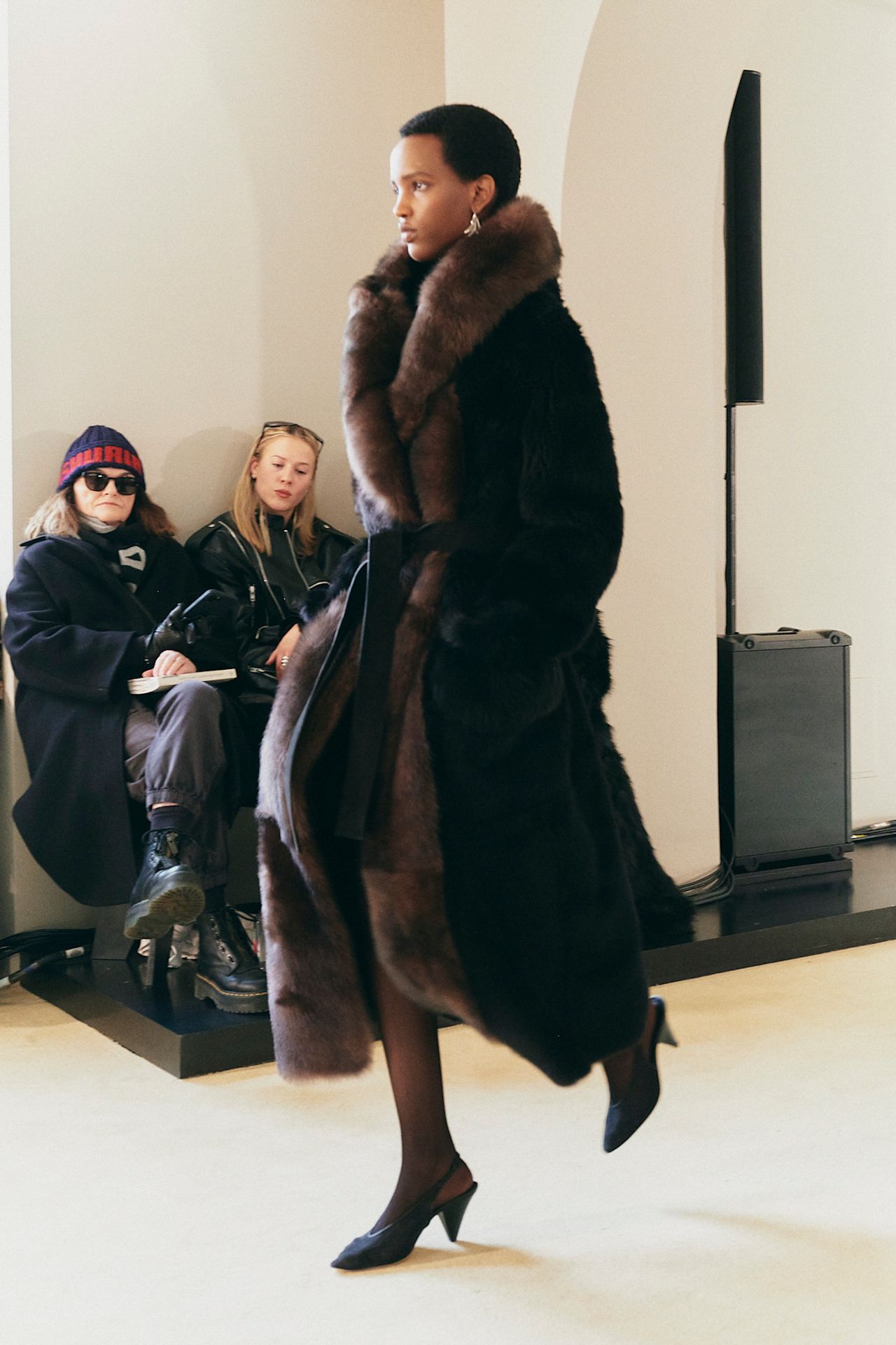 A model walking in the Altuzarra F/W 25 runway show wearing a full-length furry coat with tights and pumps.