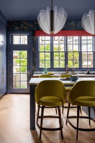 a kitchen with blue walls, yellow chairs and a red accent