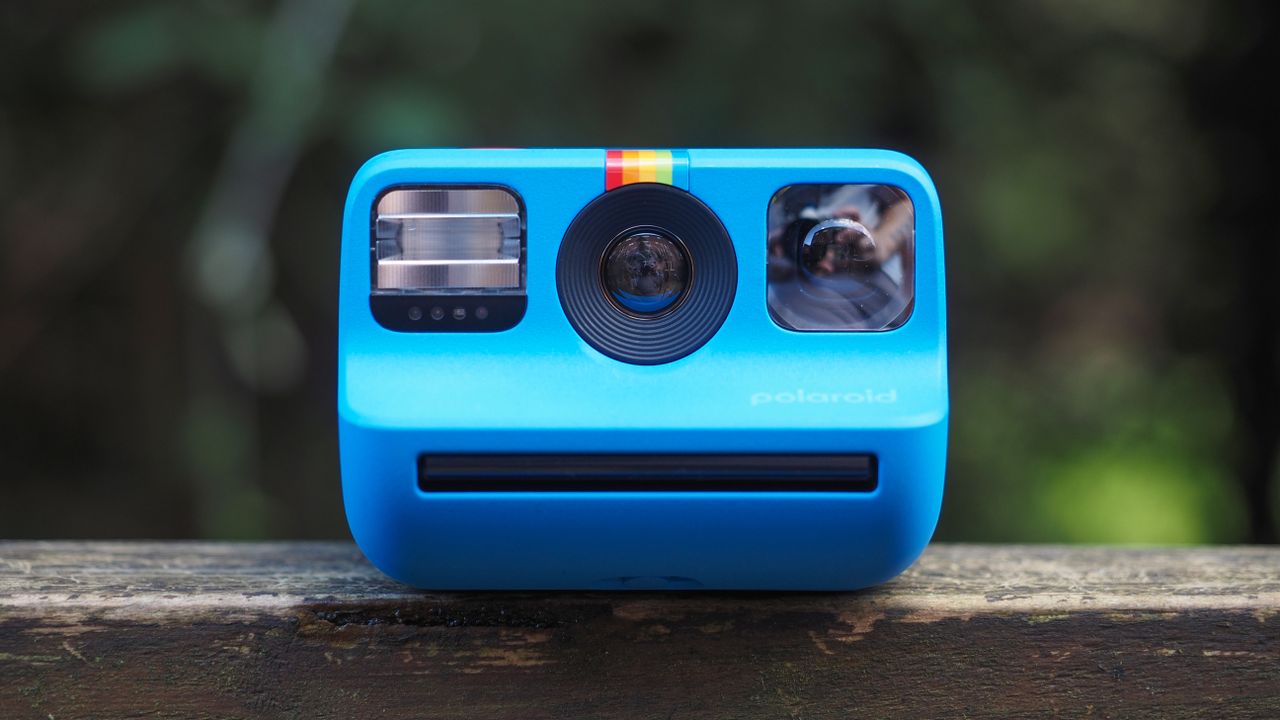 Blue Polaroid Go Gen 2 camera, on a wooden surface in a woodland setting