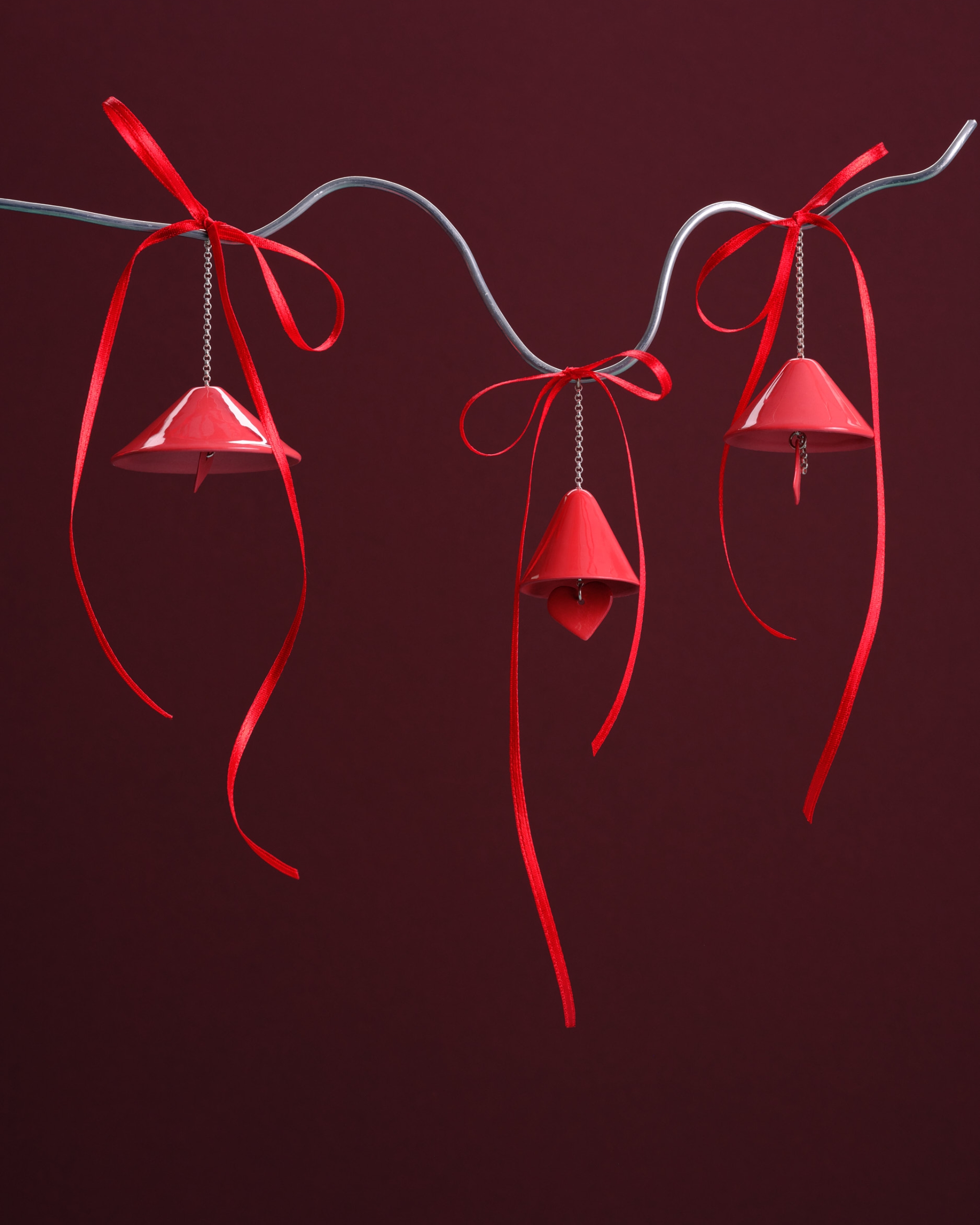 Image of three red Christmas bell ornaments hanging on a silver wire in front of a burgundy background.