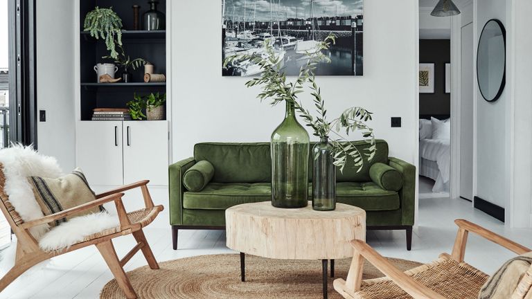 living room with white walls and green sofa with jute rug and round log coffee table green glass vases and jute armchair 
