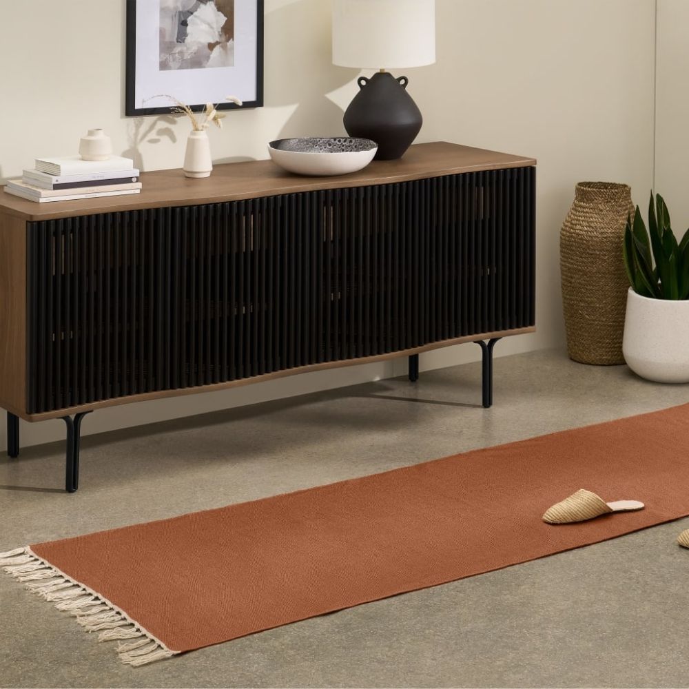 Terracotta runner on floor next to wooden sideboard and white pot with green plant inside