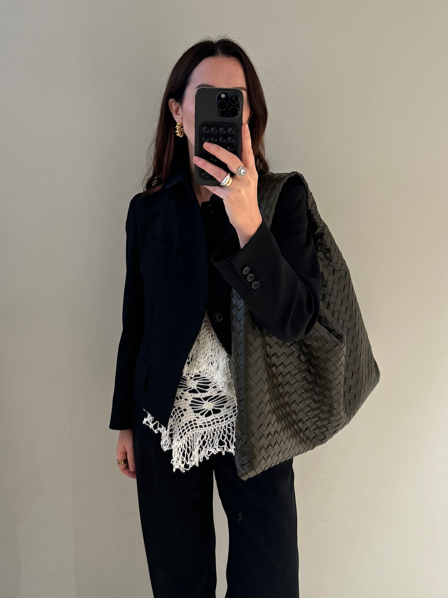 Caitlin Burke wearing a black blazer and pair of trousers with a crochet top and carrying a Bottega Veneta Hop bag.