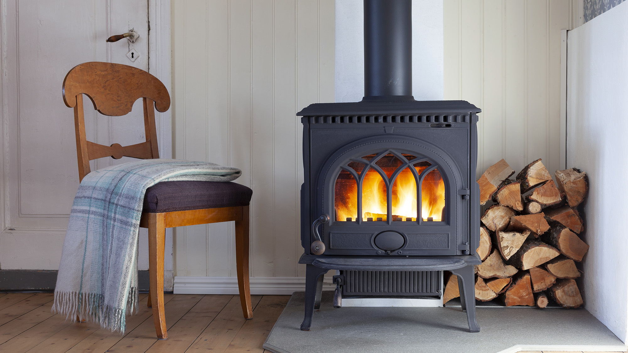 Interior with wood heating stove, chair and firewood in the corner.