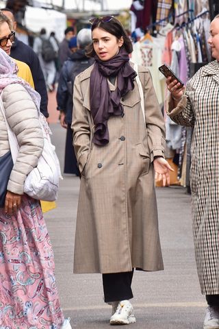 Lily Collins wearing a trench coat with Salomon sneakers.