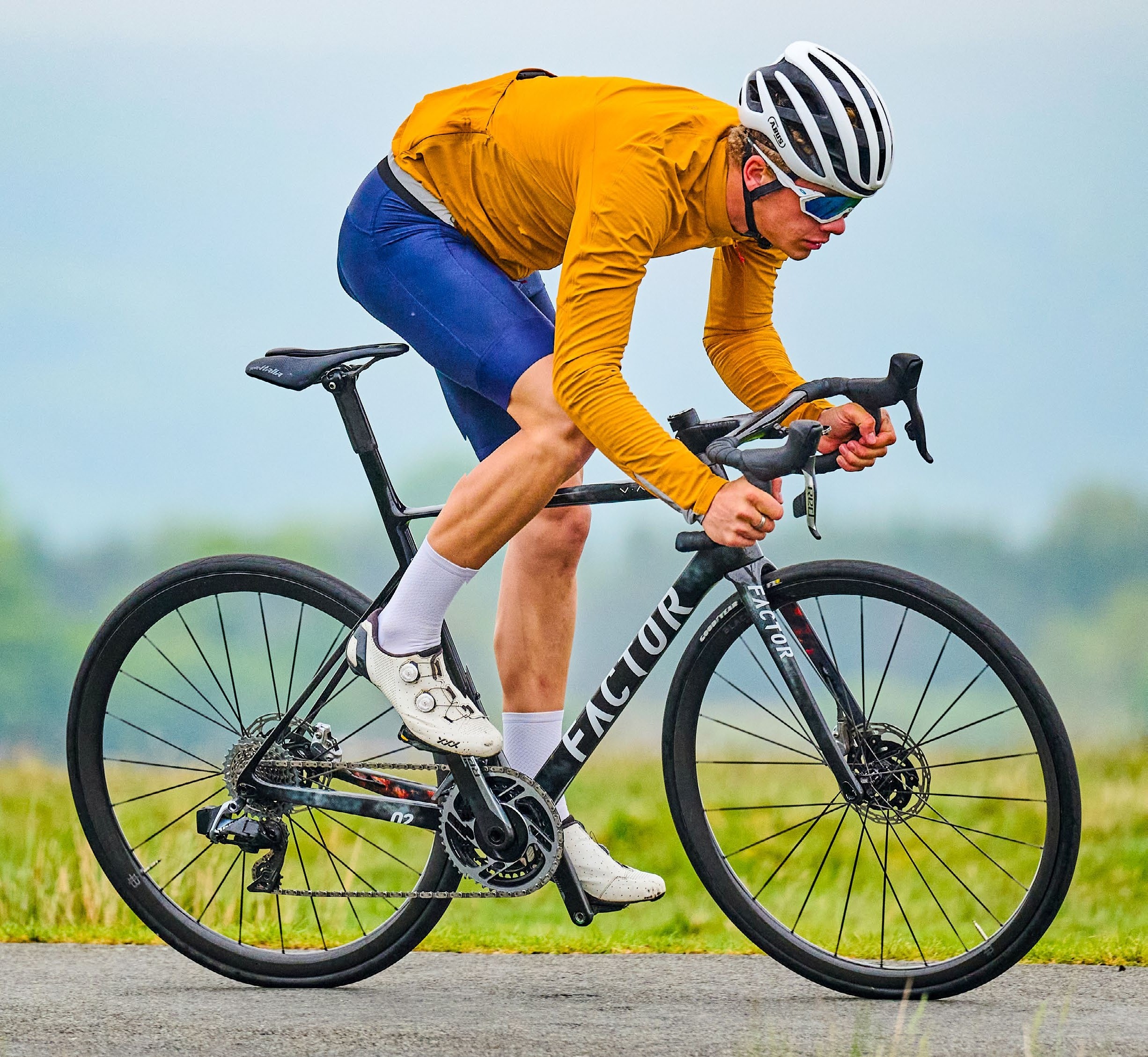 RIder in an orange jersey out of the saddle on a black Factor bike