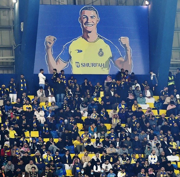 Alamy Live News. 2MD3Y40 Al Nassr fans sit under a giant billboard of Cristiano Ronaldo during the Saudi Pro League match between Al Nassr and Al Ettifaq at Mrsool Park Stadium in Riyadh, Saudi Arabia, Sunday, Jan. 22, 2023. (AP Photo)