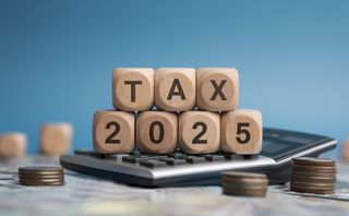 Tax 2025 written on stacked wooden blocks on top of a calculator surrounded by coins