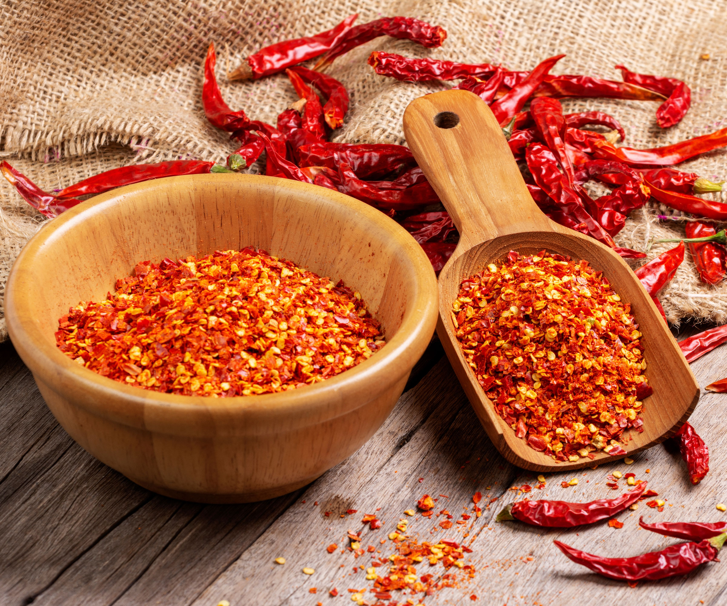 cayenne pepper seeds in wooden bowl and wooden spatula with dried peppers on hessian