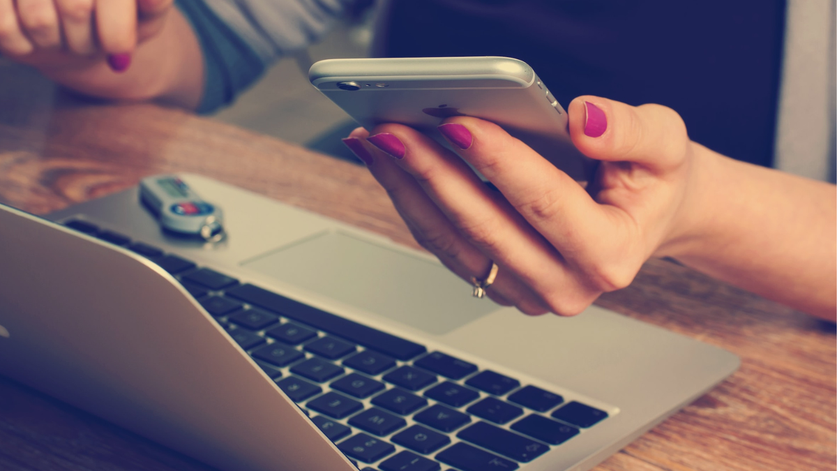 Woman on Macbook checking iPhone