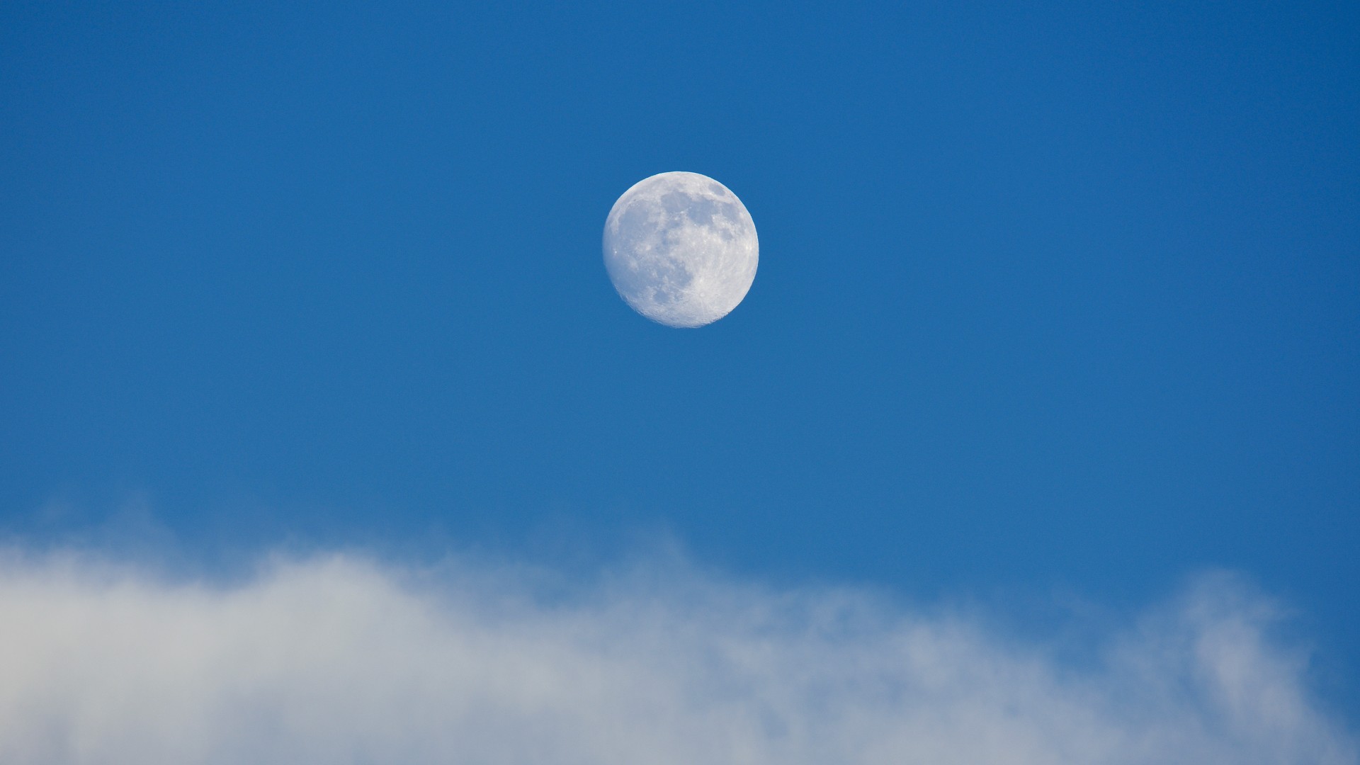 a bright full moon seen in the blue daytime sy