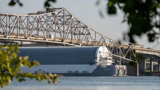 a large barge cruises under a metallic bridge spanning a river