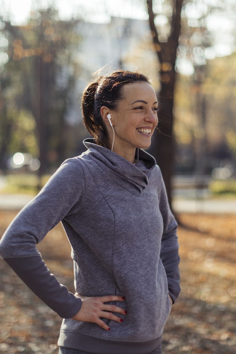 A woman in sports clothing smiles as she stands in a park