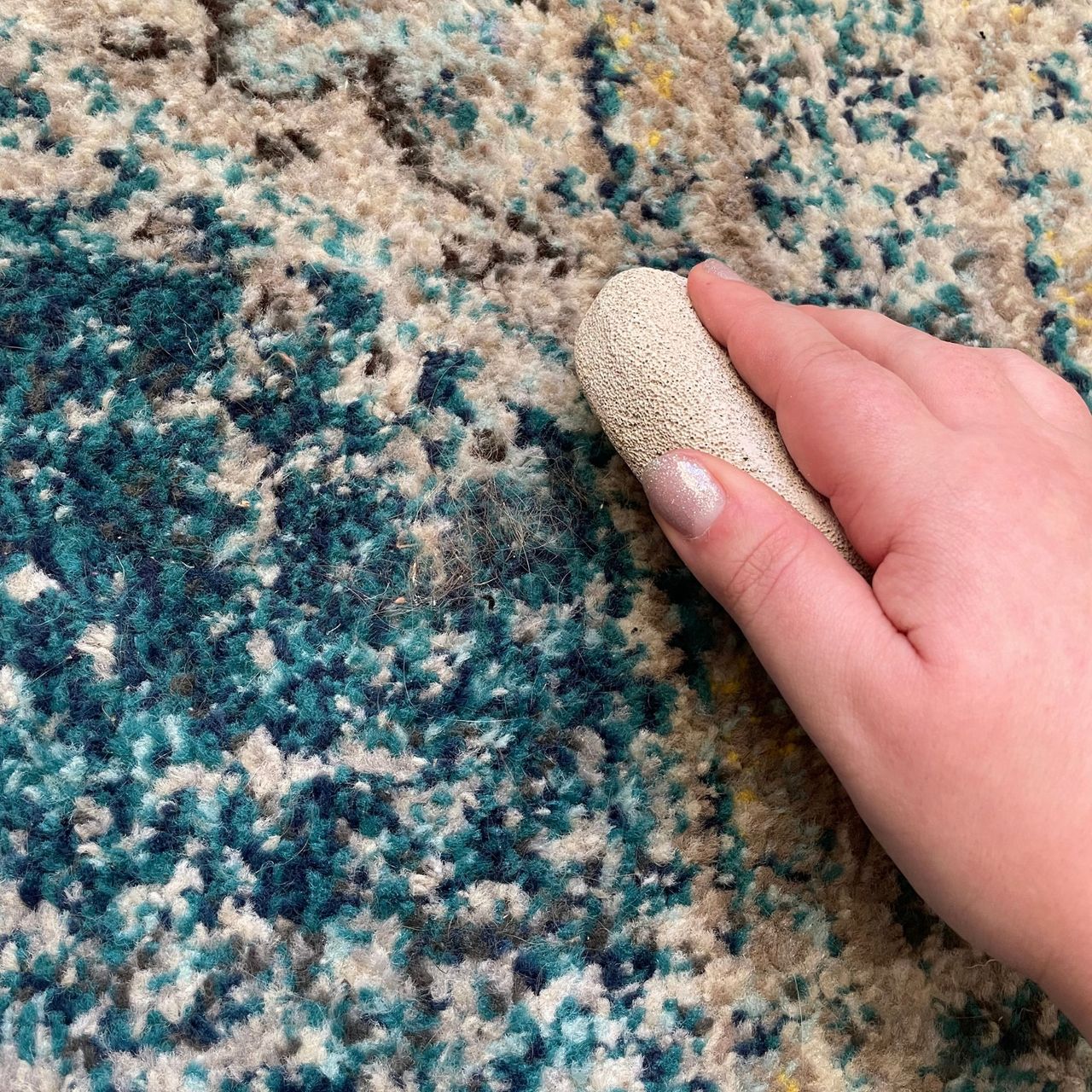 Holding a pumice stone next to some hair on a blue rug