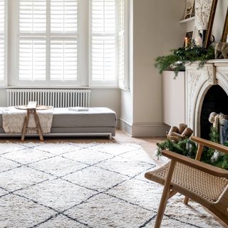 A bright living room with a Berber rug, a day bed and a fireplace, with cream walls contrasted by light taupe skirting boards