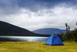 A tent is staked at the edge of a mountain lake.