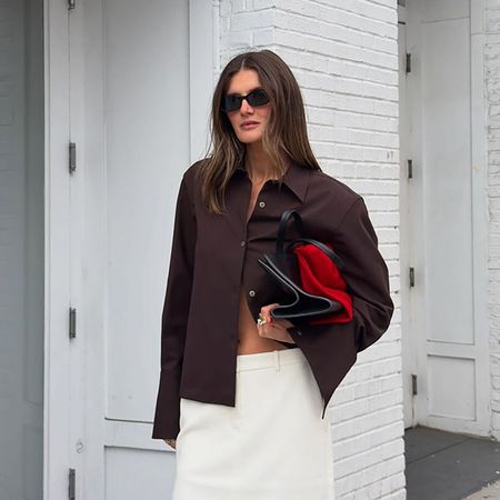 a woman wearing a brown button-down, white skirt, black clutch, and black sandals