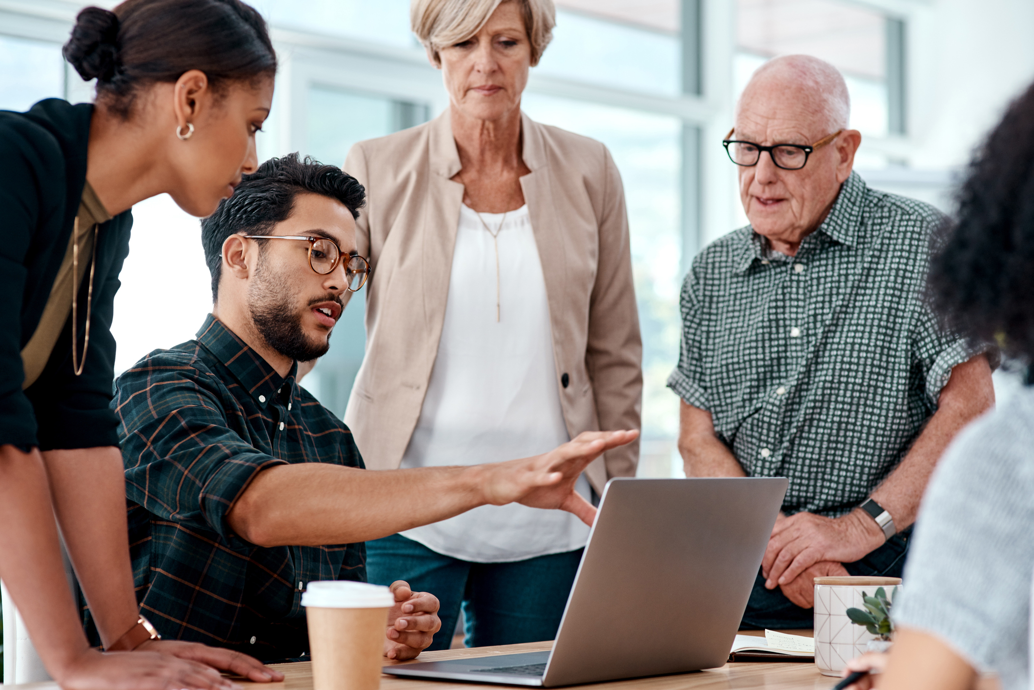 Office workers of different ages and generations gather around a computer for an informal meeting.