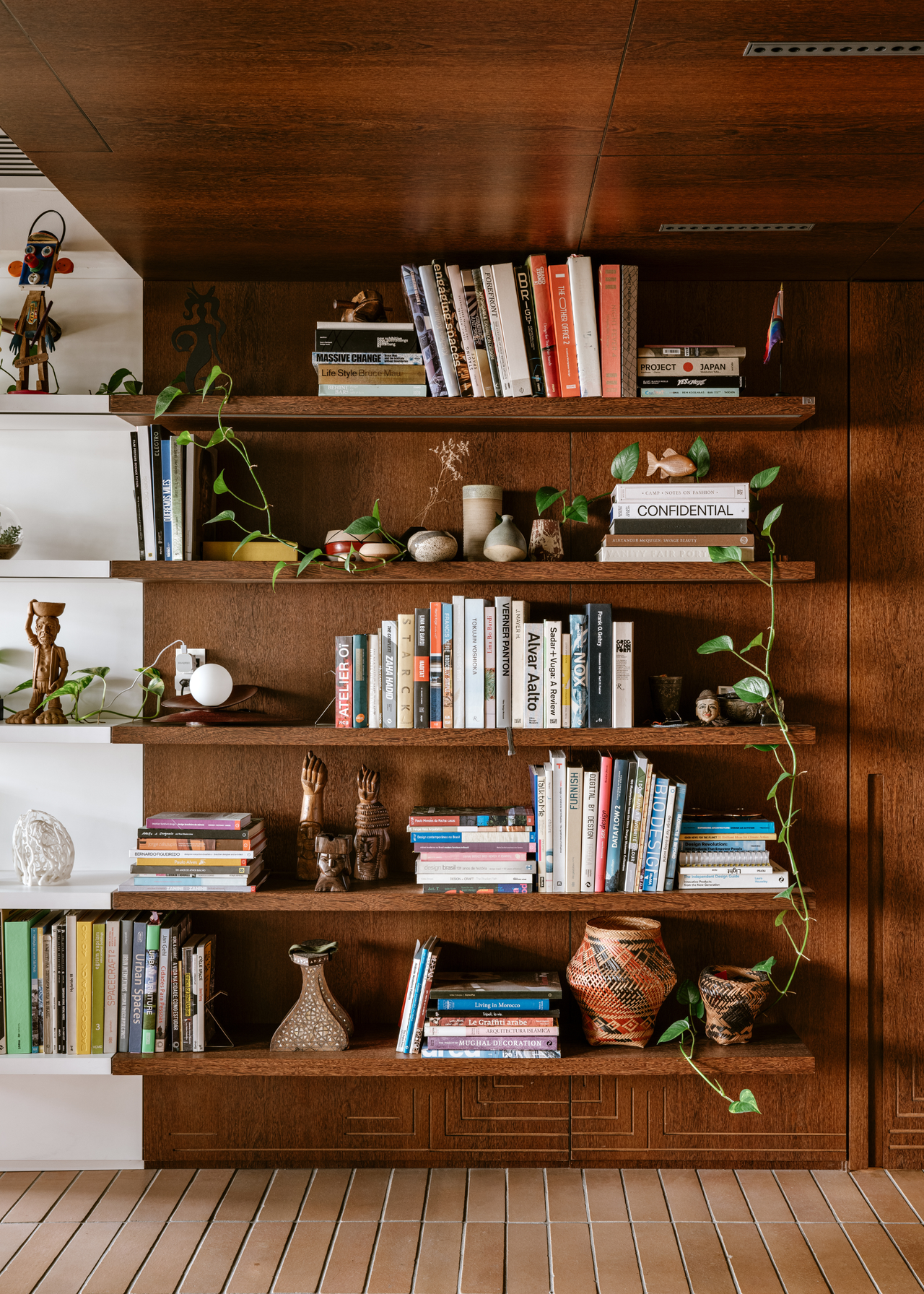 A dual-toned bookshelf with stacked books, baskets, decor and houseplants