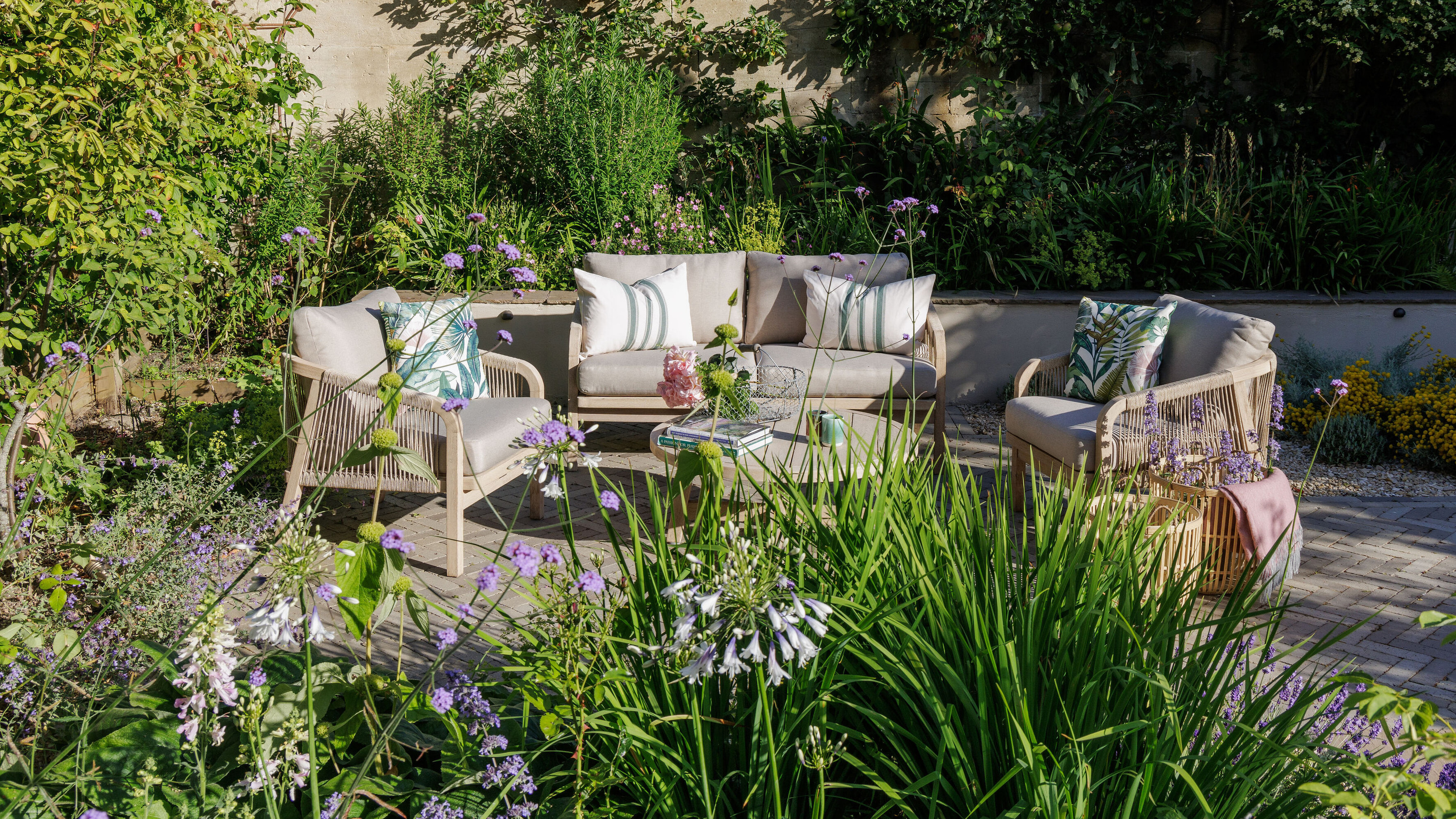 pale grey outdoor sofa and armchairs on a patio surrounded by planting