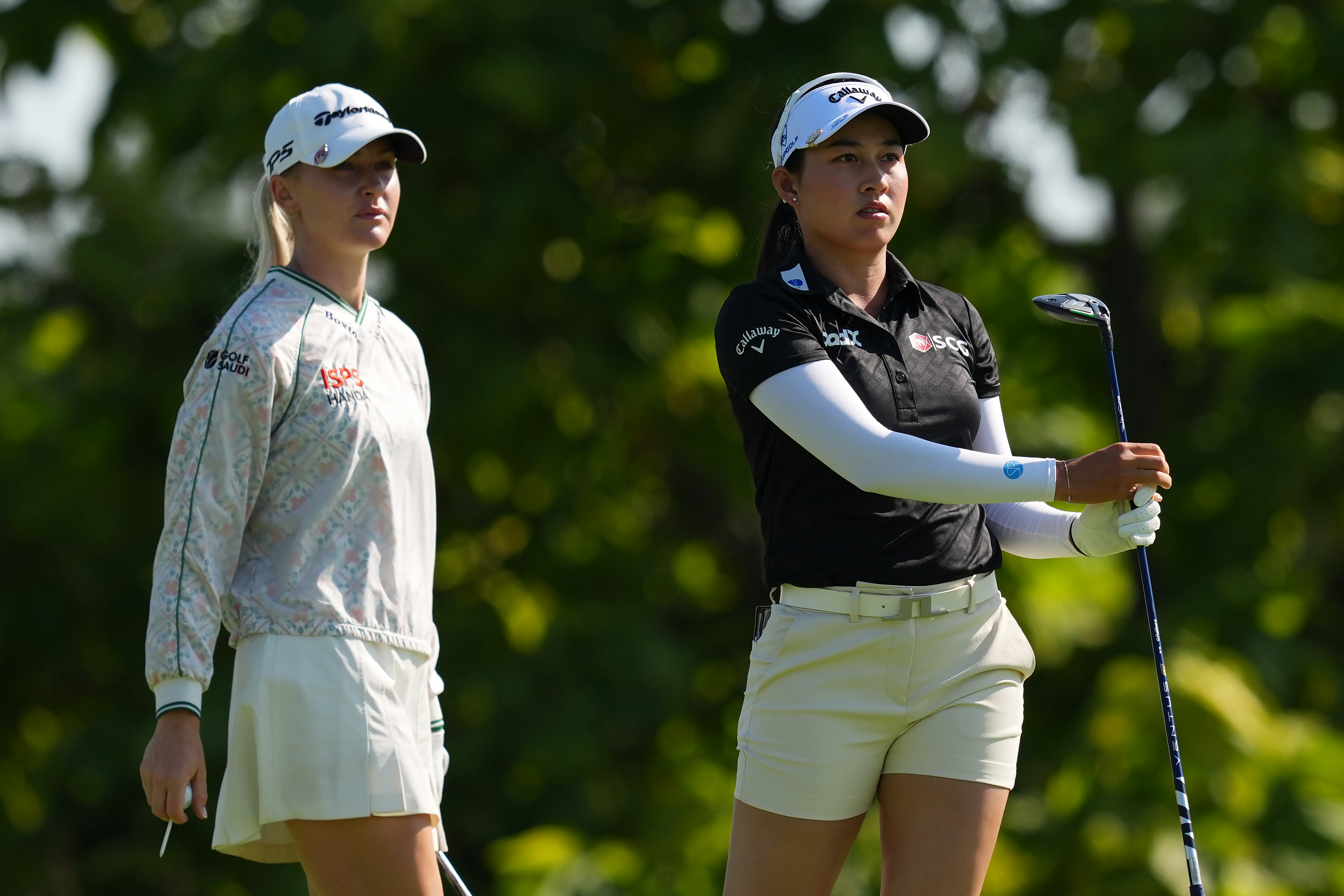 Jeeno Thitikul hits a driver off the tee, while Charley Hull stands behind her