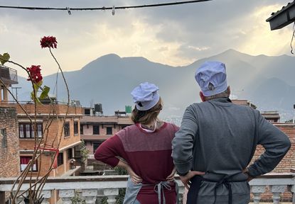 Alexandra Svokos and her father make the same pose with hands on hips looking out over a balcony in Kathmandu, Nepal, wearing chef's hats.