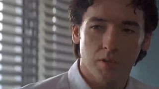 A close of John Cusack in a white shirt.